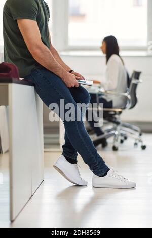 Petit coin de jeune homme d'affaires assis à la table avec un collègue travailler en arrière-plan au bureau Banque D'Images