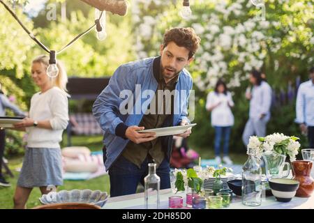 Jeune homme tenant une assiette vide à la table de salle à manger dans l'arrière-cour pendant la fête d'été Banque D'Images