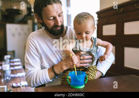 Père adulte de taille moyenne avec cuillère de mélange pour fils dans une tasse à table de restaurant Banque D'Images