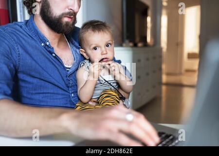 Portrait d'un bébé garçon avec un père utilisant un ordinateur portable à la maison