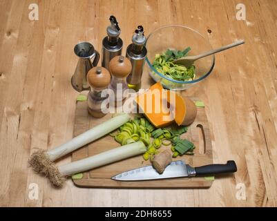 Un couteau de cuisine sur une planche à découper. Poireaux coupés en dés, courge musquée et cube de gingembre. Moulins à sel et à poivre. Bol en verre d'ingrédients et un bois s Banque D'Images