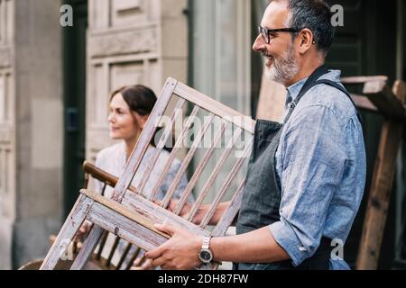 Collègues tenant des chaises en bois tout en se tenant à l'extérieur de la boutique d'antiquités Banque D'Images