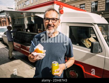 Portrait d'un client homme heureux debout contre un camion de nourriture à l'intérieur ville Banque D'Images