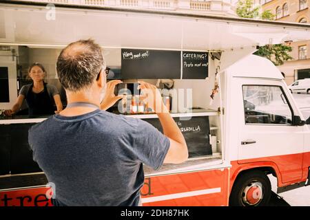 Vue arrière du propriétaire photographiant le camion de la rue en mobile téléphone Banque D'Images