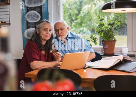 Couple senior utilisant une carte de crédit pour le paiement en ligne sur ordinateur portable à la maison Banque D'Images