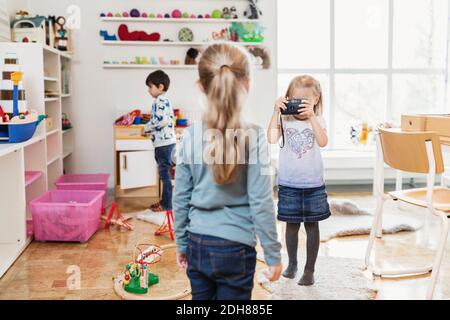 Petite fille prenant la photo d'un ami à travers un appareil photo jouet dans la salle de classe Banque D'Images