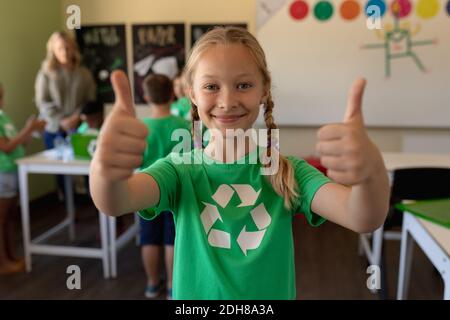 Écolière portant un t-shirt vert avec un logo de recyclage blanc dessus avec ses pouces vers le haut Banque D'Images