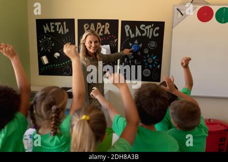 Professeur d'école féminine pointant vers une affiche de recyclage avec un groupe d'écoliers qui élèvent leur ha Banque D'Images