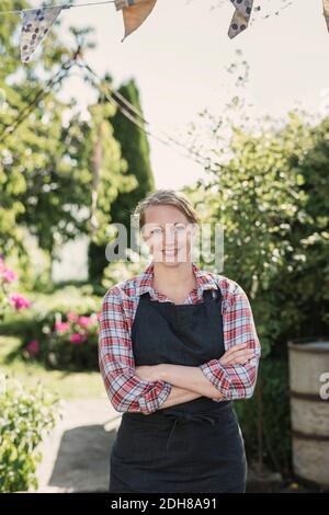 Portrait d'une femme souriante avec bras croisés debout dans le jardin Banque D'Images