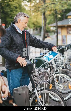 Homme senior prenant un vélo de location sur le parking Banque D'Images