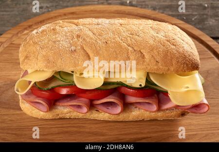 Sandwich avec un pain ciabatta, fines tranches de saucisse et fromage edam sur un plateau de bois brun Banque D'Images