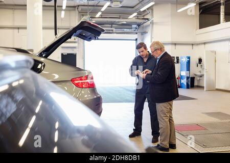 Client et mécanicien utilisant l'application mobile en voiture dans l'atelier de réparation Banque D'Images