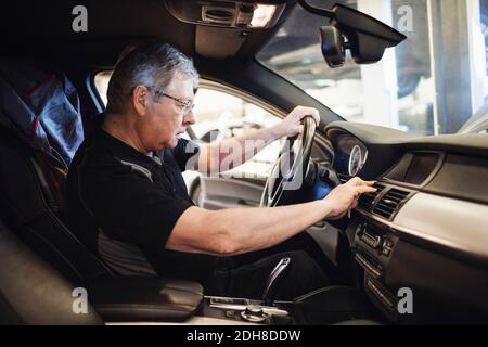 Vue latérale de l'employé senior qui examine le climatiseur en étant assis en voiture Banque D'Images