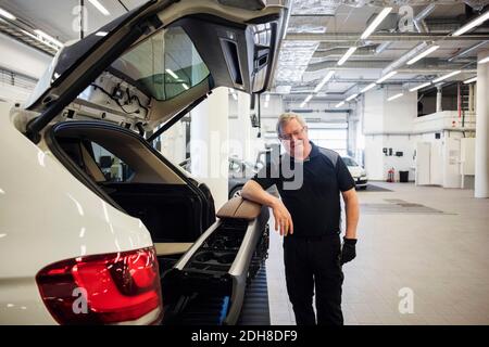 Portrait d'un mécanicien senior souriant debout en voiture atelier de réparation Banque D'Images