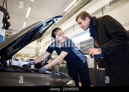 Femme mécanicien répare la voiture en regardant le client dans l'automobile atelier de réparation Banque D'Images