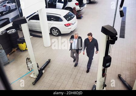 Vue en grand angle de l'homme senior discutant avec le mécanicien pendant dans un atelier de réparation automobile Banque D'Images