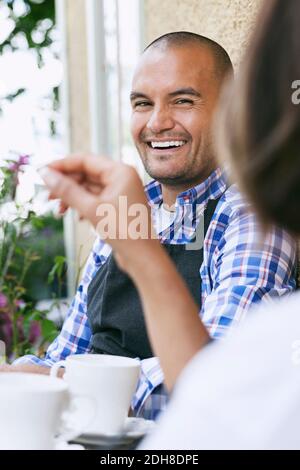 Homme souriant avec une collègue de travail assis à table devant le café Banque D'Images