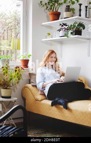 Femme souriante utilisant un ordinateur portable tout en se reposant sur une chaise longue à accueil Banque D'Images