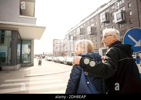 Vue arrière du couple senior marchant dans la rue de la ville contre ciel dégagé Banque D'Images