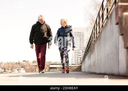 Couple senior de sportswear marchant sur un trottoir dans un ciel dégagé Banque D'Images