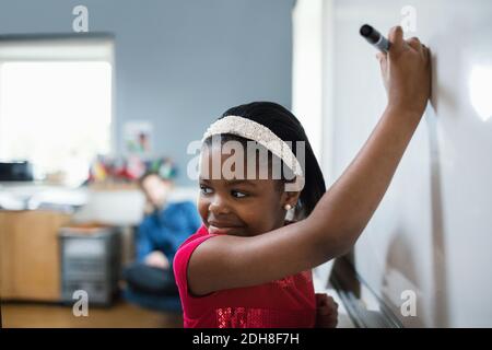 Gros plan d'une fille regardant sur l'épaule tout en écrivant sur un tableau blanc en classe Banque D'Images