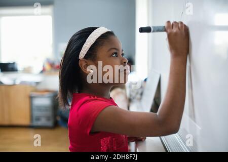 Vue latérale gros plan d'une fille écrivant sur un tableau blanc en classe Banque D'Images