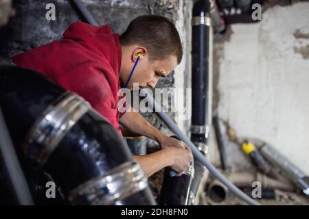 Plombier concentré travaillant sur les tuyaux tout en écoutant de la musique au sous-sol Banque D'Images