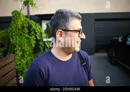 Homme souriant portant des lunettes debout contre la maison Banque D'Images