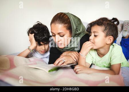 Mère lisant le livre aux garçons tout en étant couché sur le lit à accueil Banque D'Images