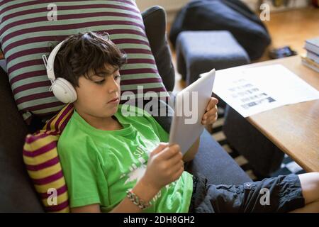 Garçon écoutant de la musique sur une tablette numérique tout en étant assis sur un canapé à la maison Banque D'Images