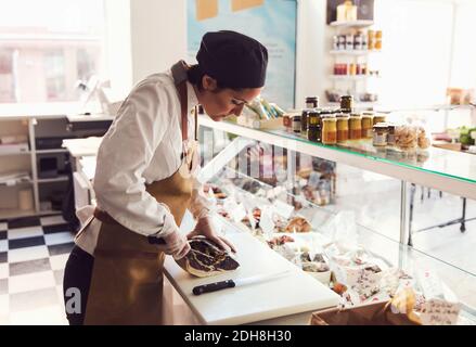 Femme propriétaire coupant de la viande au comptoir de l'épicerie Banque D'Images