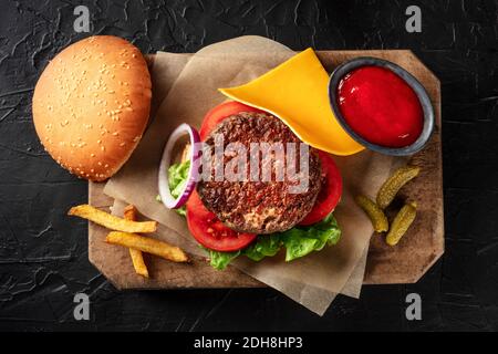 Hamburger avec du bœuf, du fromage, de l'oignon, de la tomate et de la salade verte, avec un petit pain et du ketchup, avec des frites, tiré d'en haut Banque D'Images