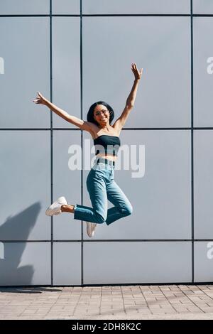 Portrait de fille noire positive gaie sautant dans l'air sur fond de rue murale Banque D'Images