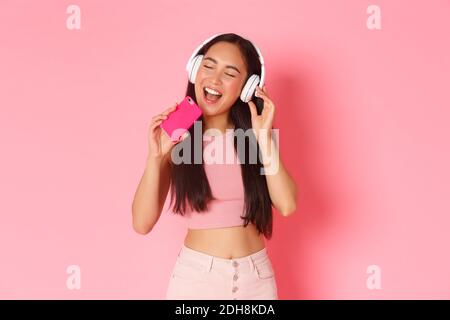 Portrait à la taille haute d'une jolie fille asiatique proche des yeux et chantant le long d'une chanson tout en écoutant de la musique dans un casque ou un lecteur Banque D'Images