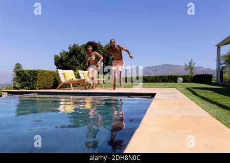 Un jeune couple sautant sur la piscine une journée ensoleillée Banque D'Images