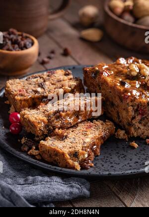 Pain de gâteau aux fruits coupé en tranches sur une assiette avec raisins secs et noix en arrière-plan sur une table rustique en bois Banque D'Images