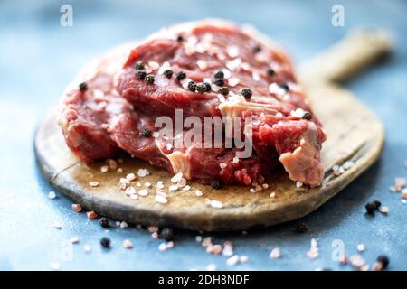 Steak de bœuf cru à la viande sur planche à découper en bois, sel de l'Himalaya rose grossier et poivre noir Banque D'Images