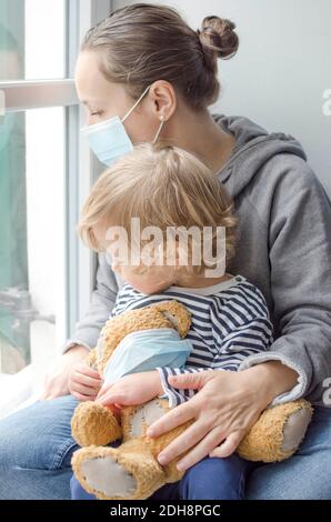 Mère et enfant en quarantaine à domicile en regardant par la fenêtre, portant un masque médical contre les virus pendant le coronavirus COVID-2019 et la grippe verrouillée. Se Banque D'Images