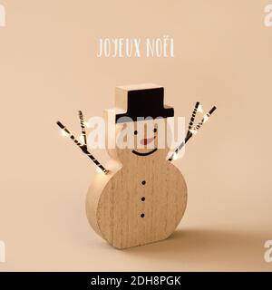 un bonhomme de neige en bois drôle, avec un nez rouge et un chapeau, et le texte joyeux noël en français sur fond marron pâle Banque D'Images