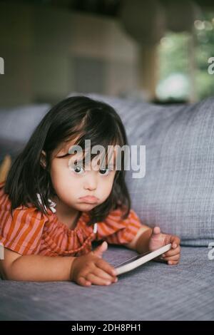 Portrait d'une fille atteinte du syndrome de Down à l'aide d'une tablette numérique en position allongée sur le canapé à la maison Banque D'Images