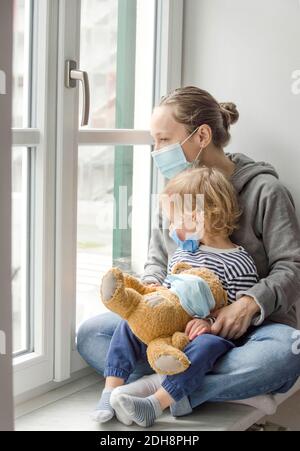 Mère et enfant en quarantaine à domicile en regardant par la fenêtre, portant un masque médical contre les virus pendant le coronavirus COVID-2019 et la grippe verrouillée. Se Banque D'Images