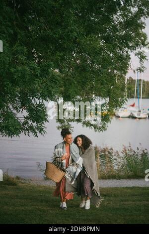 Mère et fille souriantes marchant sur des terres herbeuses contre le lac au coucher du soleil Banque D'Images