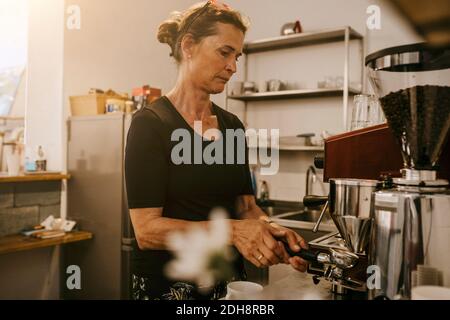 Une femme senior prépare un café dans un café Banque D'Images