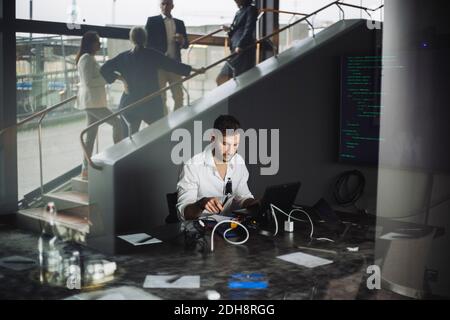 Professionnel travaillant sur un ordinateur portable pendant que ses collègues discutent en escalier dans le bureau créatif Banque D'Images