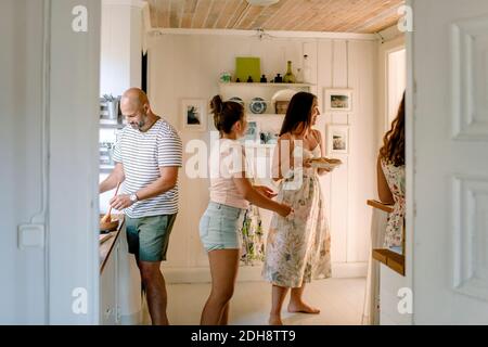 Une mère et des filles souriantes s'amusent tout en préparant la nourriture dans la cuisine Banque D'Images