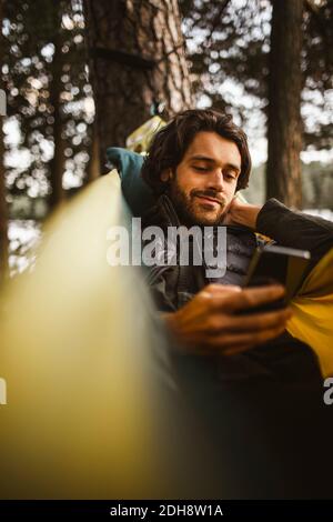 Jeune homme utilisant un téléphone portable en se reposant sur un hamac forêt Banque D'Images