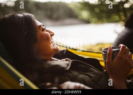 Femme souriante avec un café qui donne sur un hamac en forêt pendant les vacances Banque D'Images