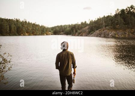 Vue arrière de l'homme debout près du lac en forêt pendant vacances Banque D'Images