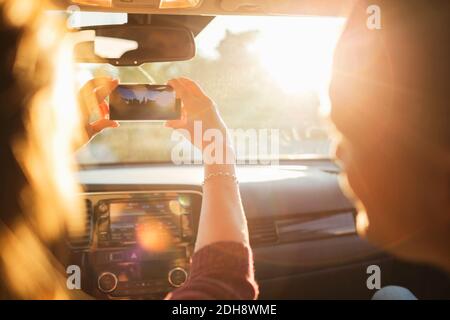 Homme regardant une femme qui photographie depuis un téléphone portable en voiture pare-brise Banque D'Images