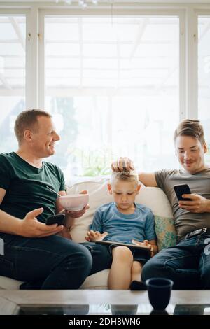 Des pères souriants parlent pendant que leur fils utilise une tablette numérique à la maison Banque D'Images